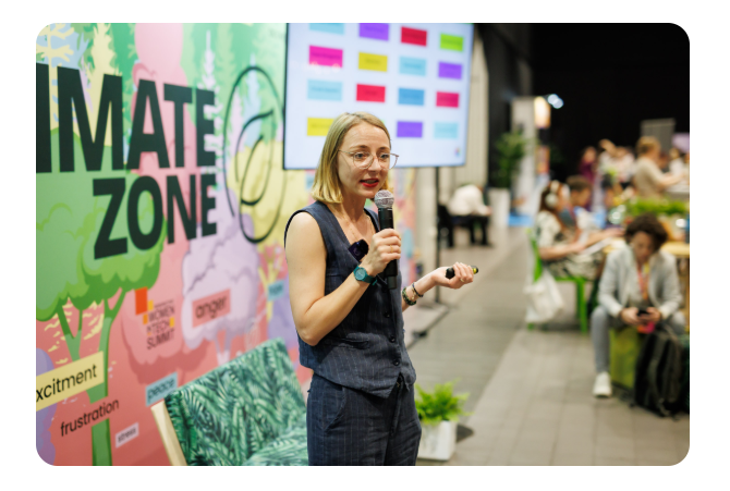 Magda Kufrej presenting with a microphone beside a colorful Mate Zone wall